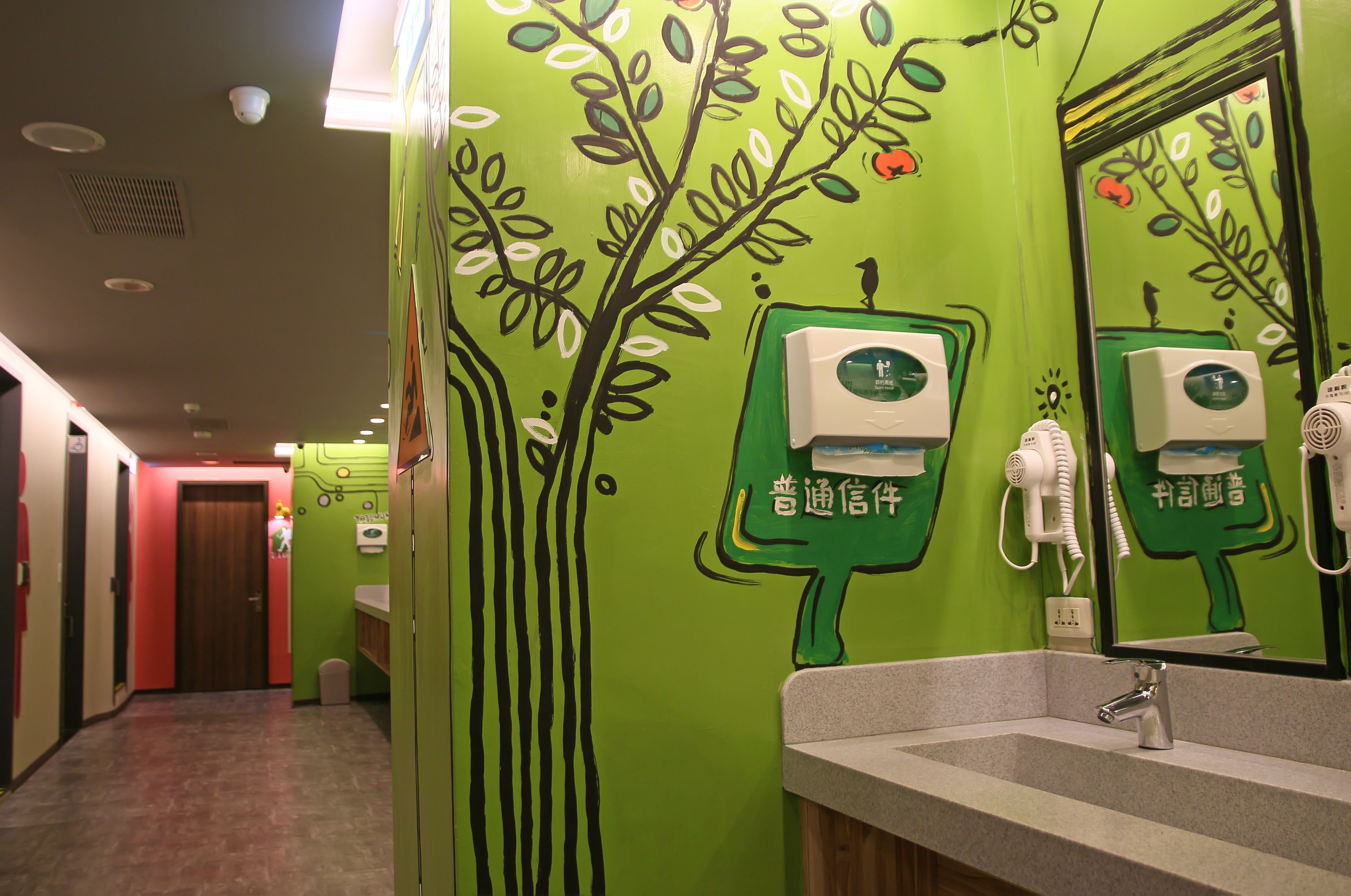 A bathroom with green walls, a sink, and a mirror. There are hand dryers and a paper towel dispenser.