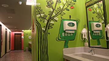 A bathroom with green walls, a sink, and a mirror. There are hand dryers and a paper towel dispenser.