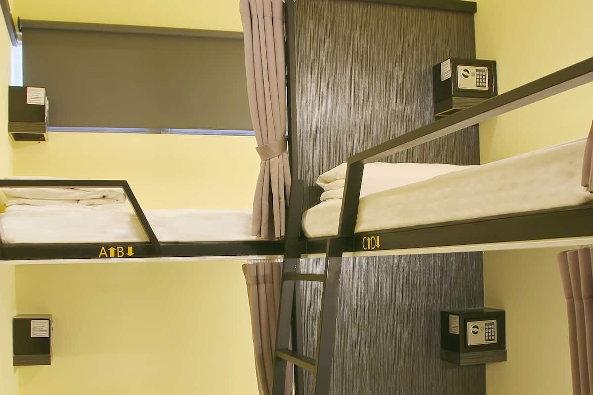 A bunk bed room with a wooden ladder, a small shelf with a lock, and a window with curtains.