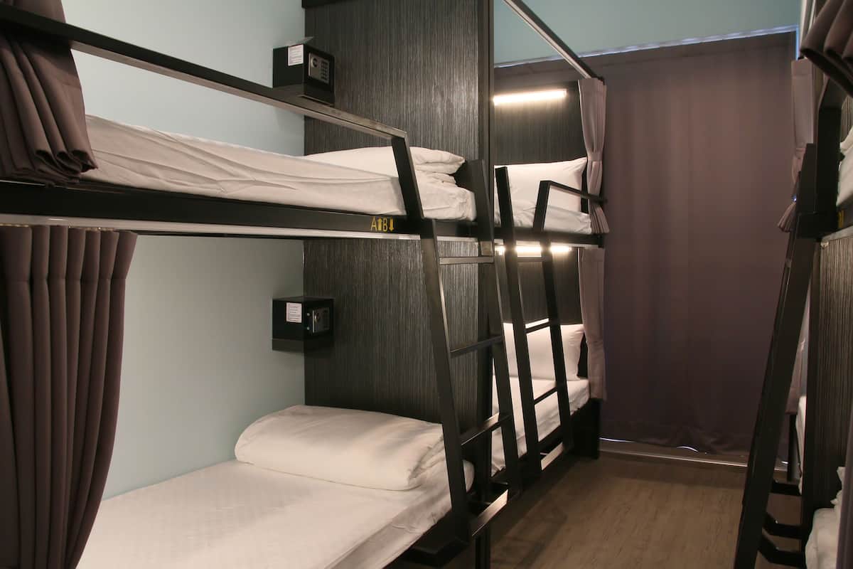A bunk bed room with a wooden floor, a wall-mounted light, and a curtain.