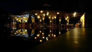 A nighttime view of a building with a reflective pool, illuminated by hanging lights.