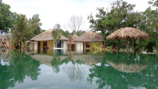 A pool with thatched-roof huts and palm trees.