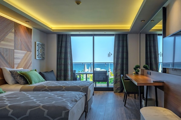 Quarto de hotel moderno com uma cama grande, uma escrivaninha e uma varanda com vista para o mar.