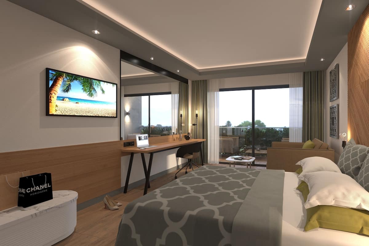 A modern hotel room with a large bed, a desk, and a balcony with a view of the city.
