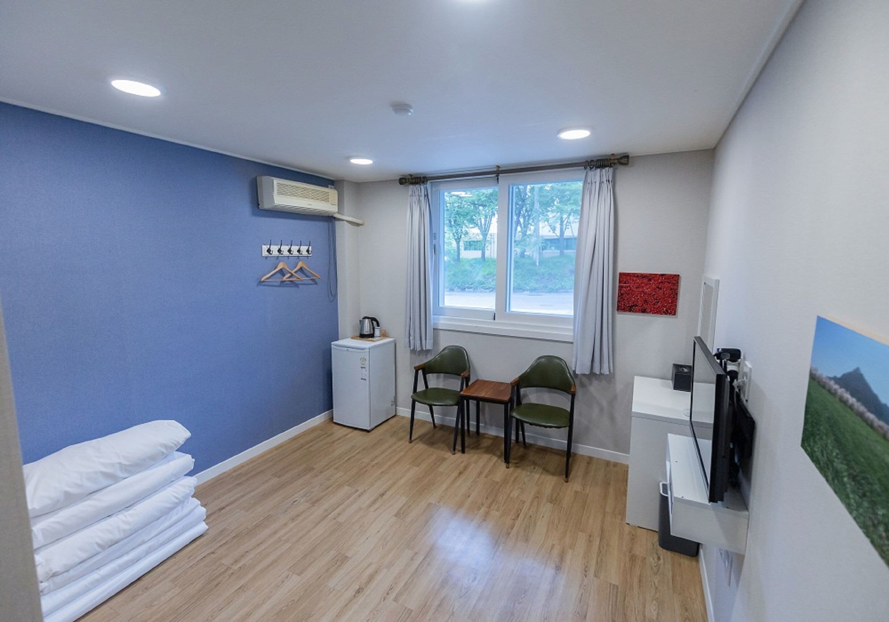 A room with a bed, a desk, a chair, a small kitchenette, and a window with curtains.