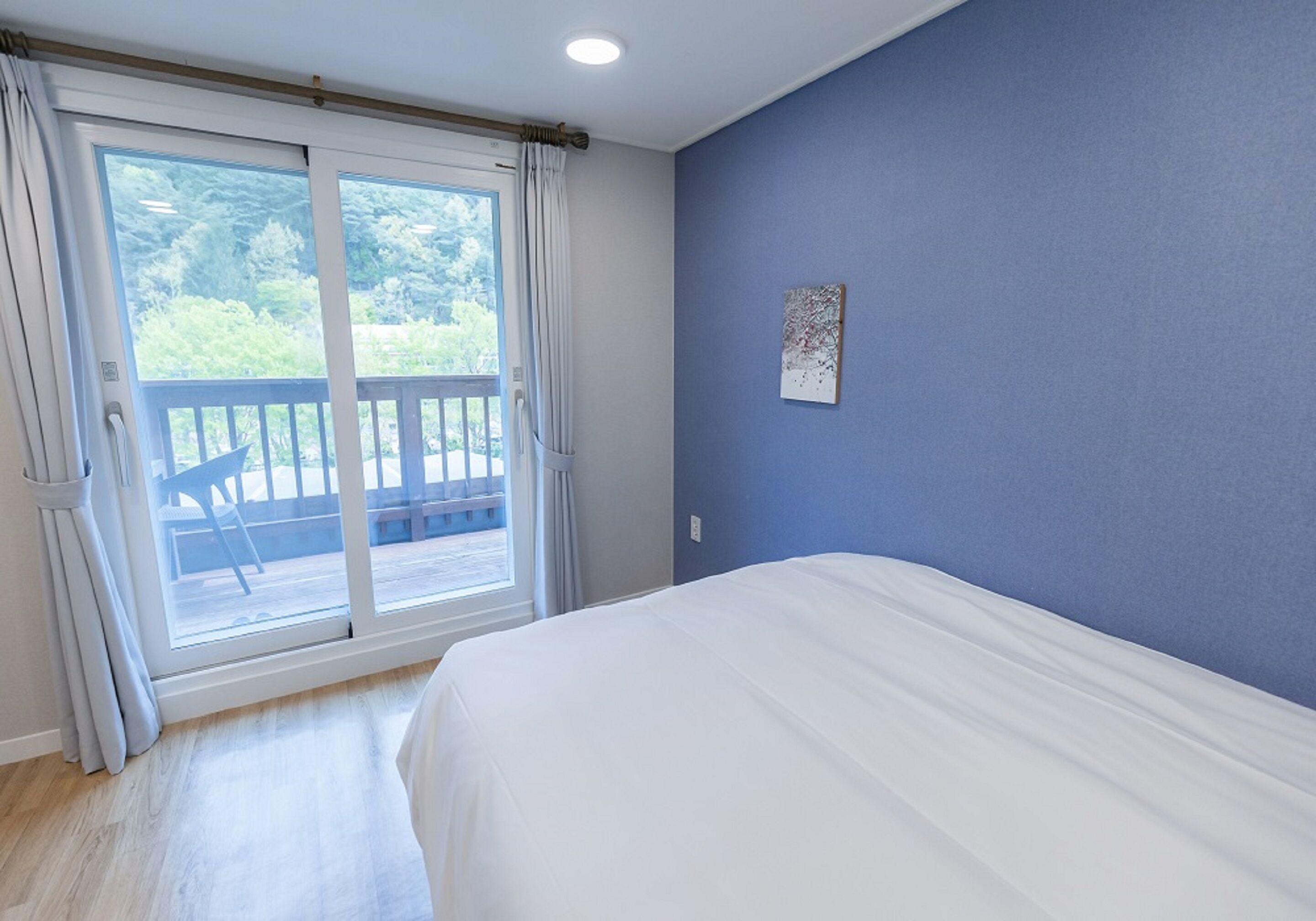 A bedroom with a large bed, a sliding glass door leading to a balcony, and a blue wall.