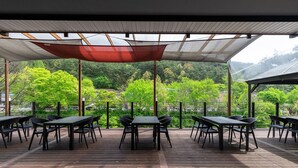 Un patio al aire libre con mesas y sillas, un toldo arriba y vistas a un área boscosa.