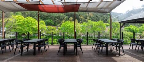 Un patio al aire libre con mesas y sillas, un toldo arriba y vistas a un área boscosa.