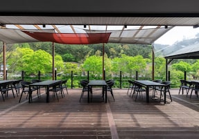 Un patio al aire libre con mesas y sillas, un toldo arriba y vistas a un área boscosa.