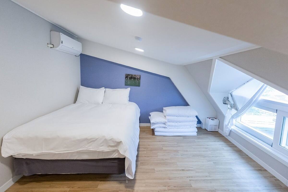 Een slaapkamer met een bed, een blauwe accentmuur, een raam en een plafondventilator.