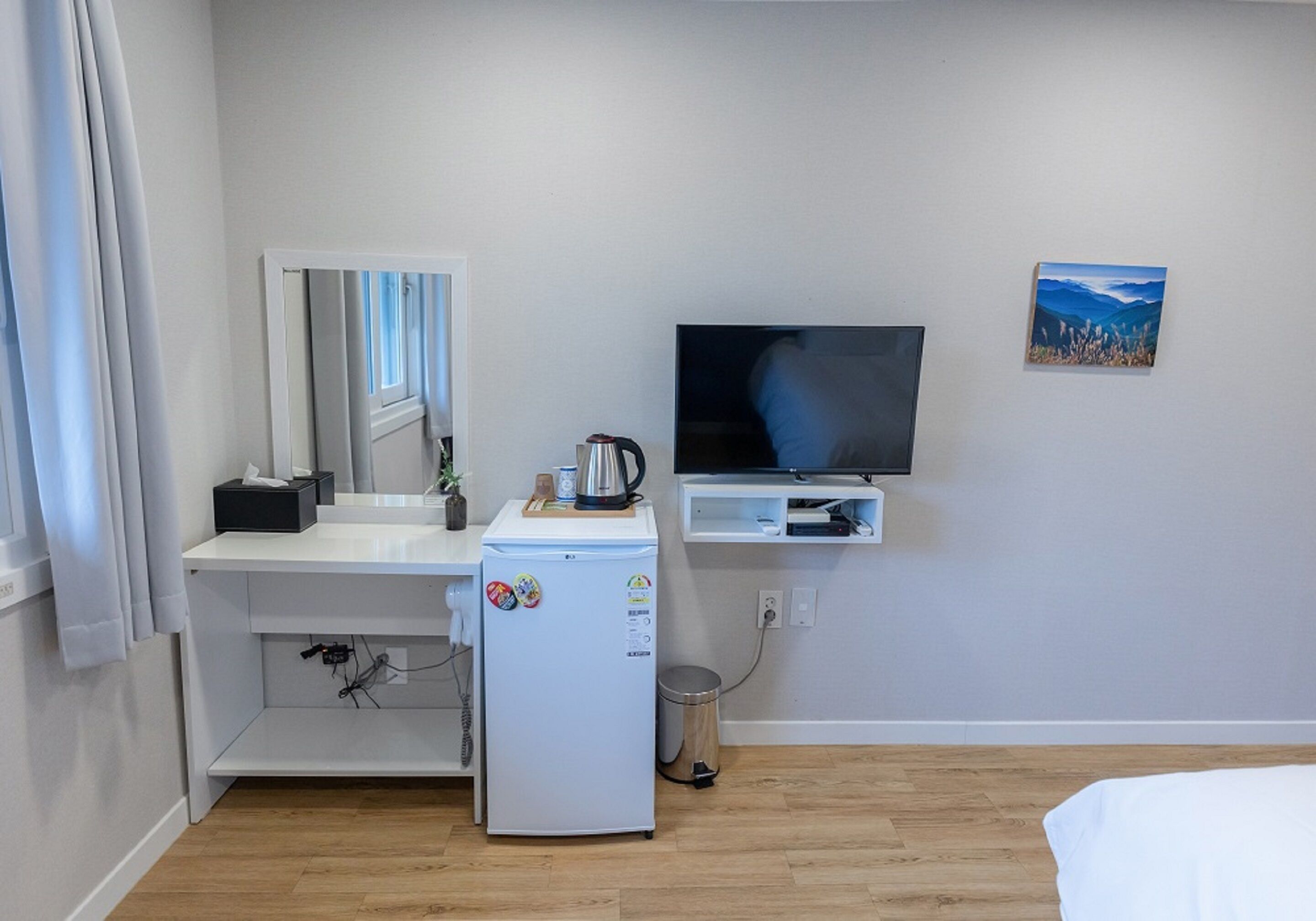 Habitación de hotel compacta con kitchenette, televisor y un estante pequeño.