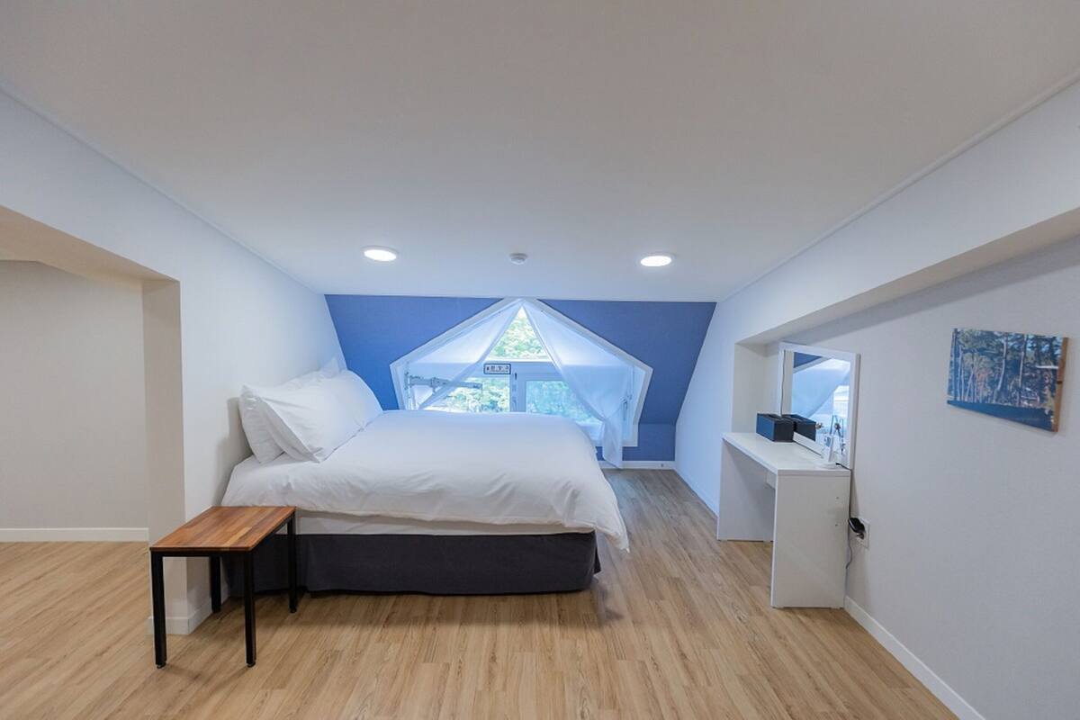 Een slaapkamer met een bed, een bureau en een raam met uitzicht op groen.