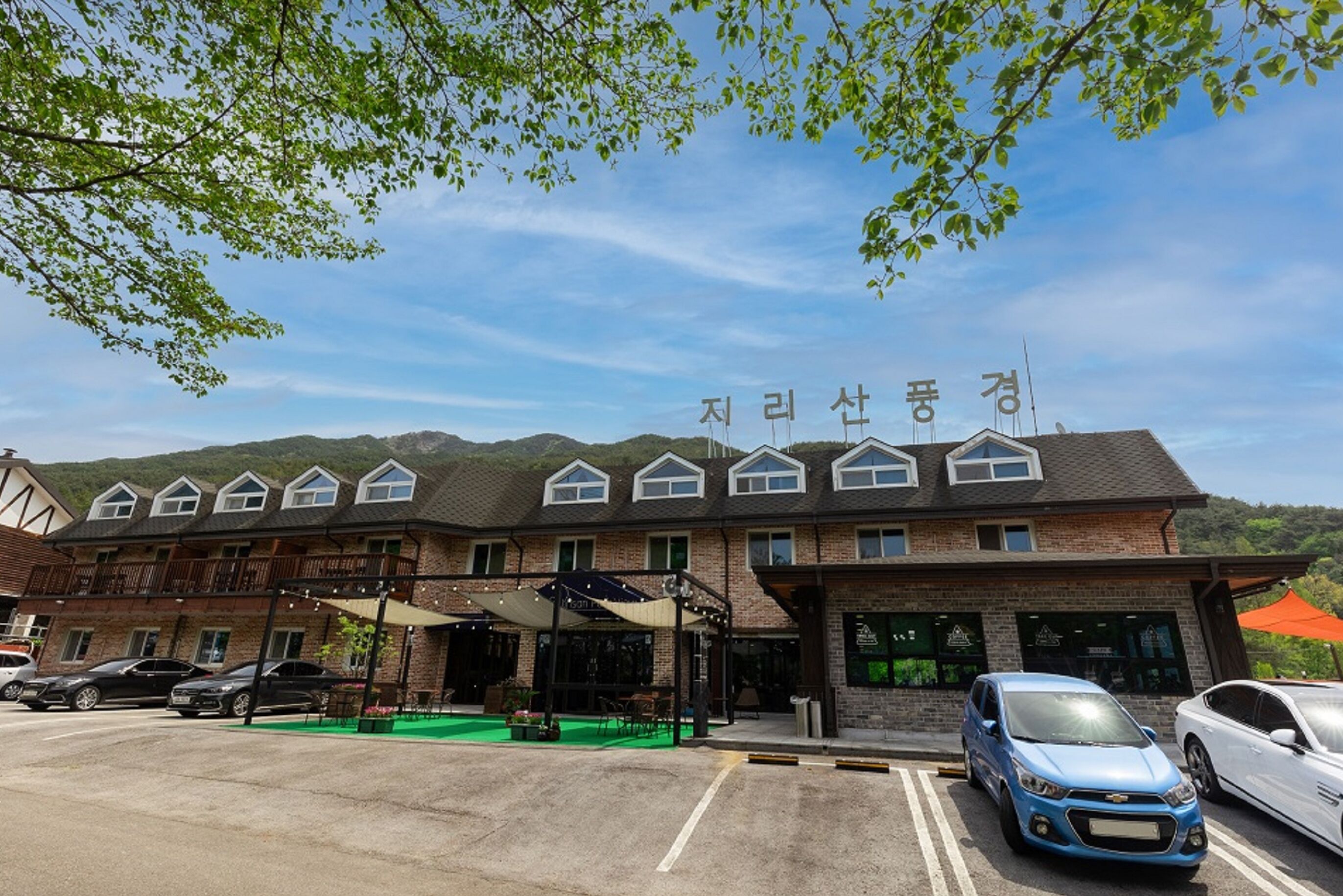 Un hotel de fachada de ladrillo, con varias ventanas y un estacionamiento con varios coches.