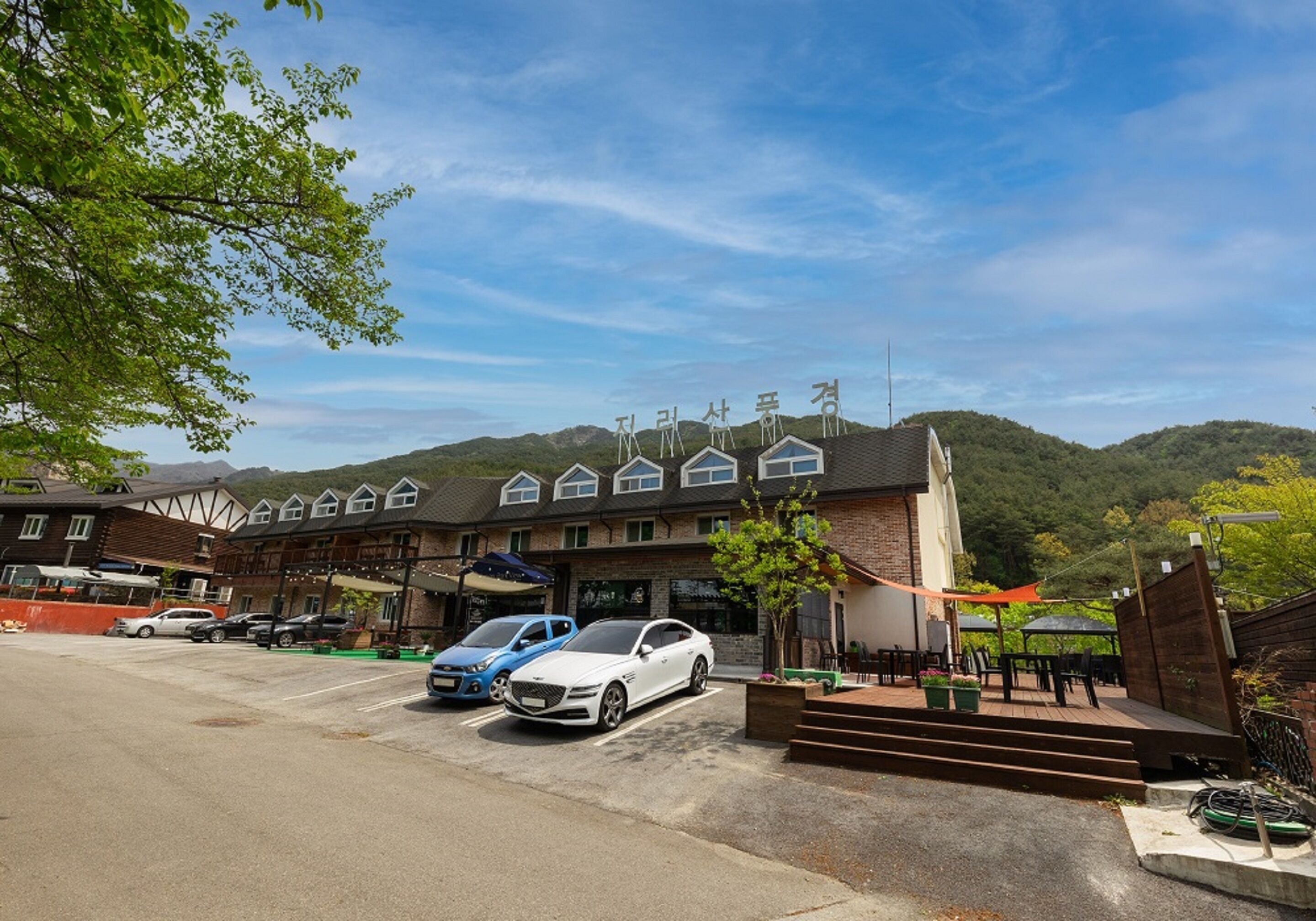 Un hotel con un estacionamiento, un coche blanco y un coche azul estacionados al frente.
