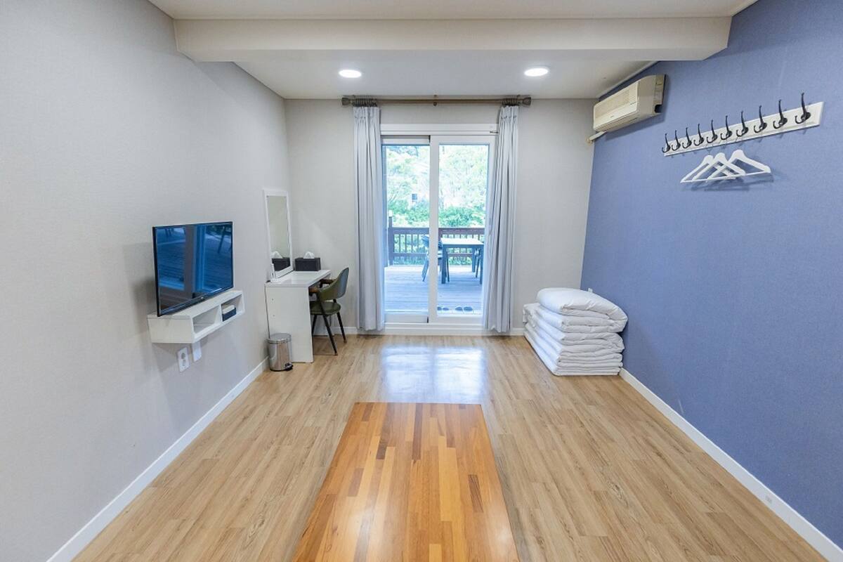 Een hotelkamer met een houten vloer, een televisie, een bureau met stoel, een balkon met uitzicht en een stapel handdoeken.