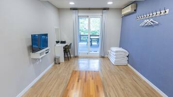 A hotel room with a wooden floor, a TV, a desk with a chair, a balcony with a view, and a stack of towels.