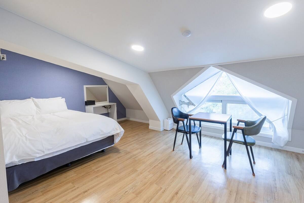 Een slaapkamer met een bed, bureau en stoel, dakraam en uitzicht op de omgeving.
