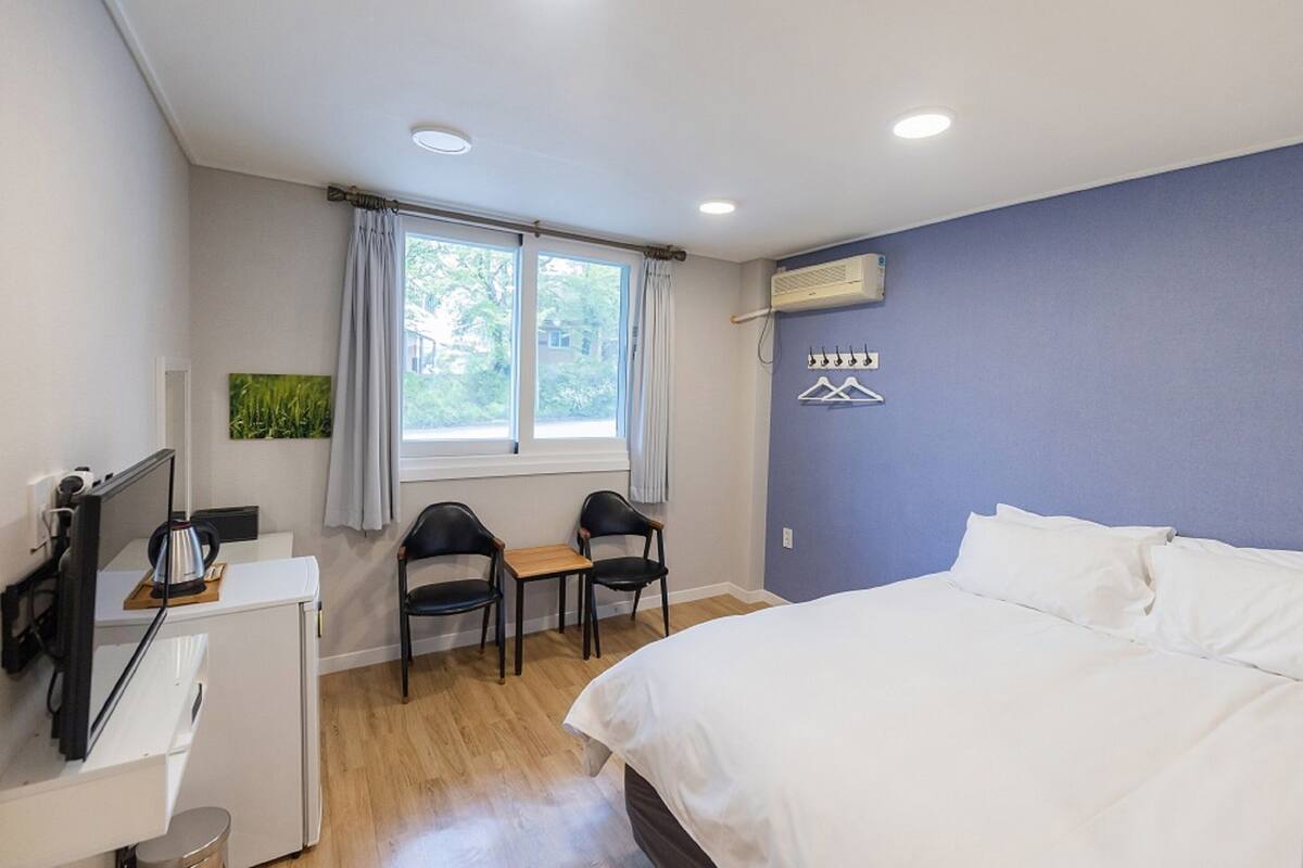Een hotelkamer met een bed, een bureau met stoel, een televisie en een airconditioner.