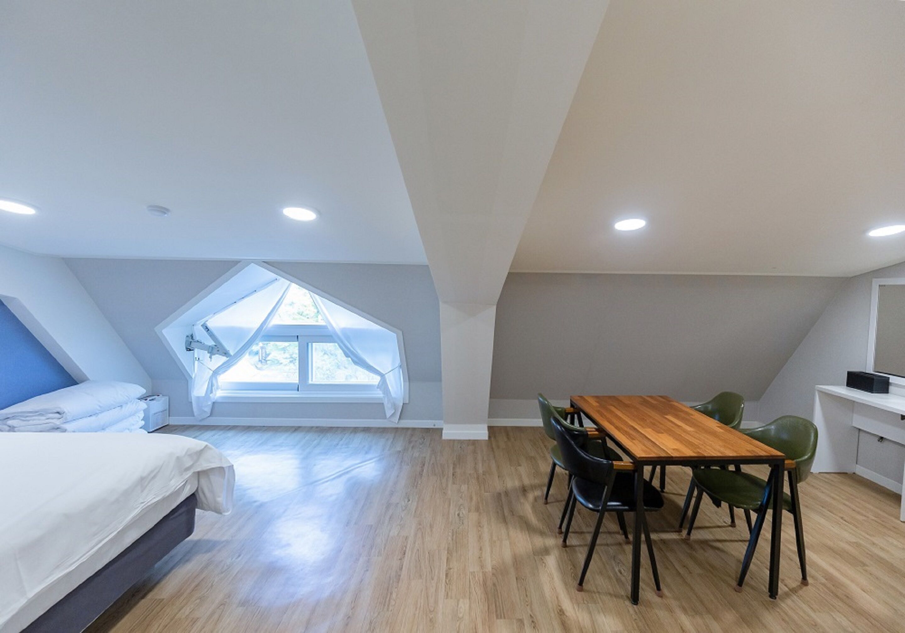 A bedroom with a skylight, a wooden dining table with chairs, and a small kitchenette.