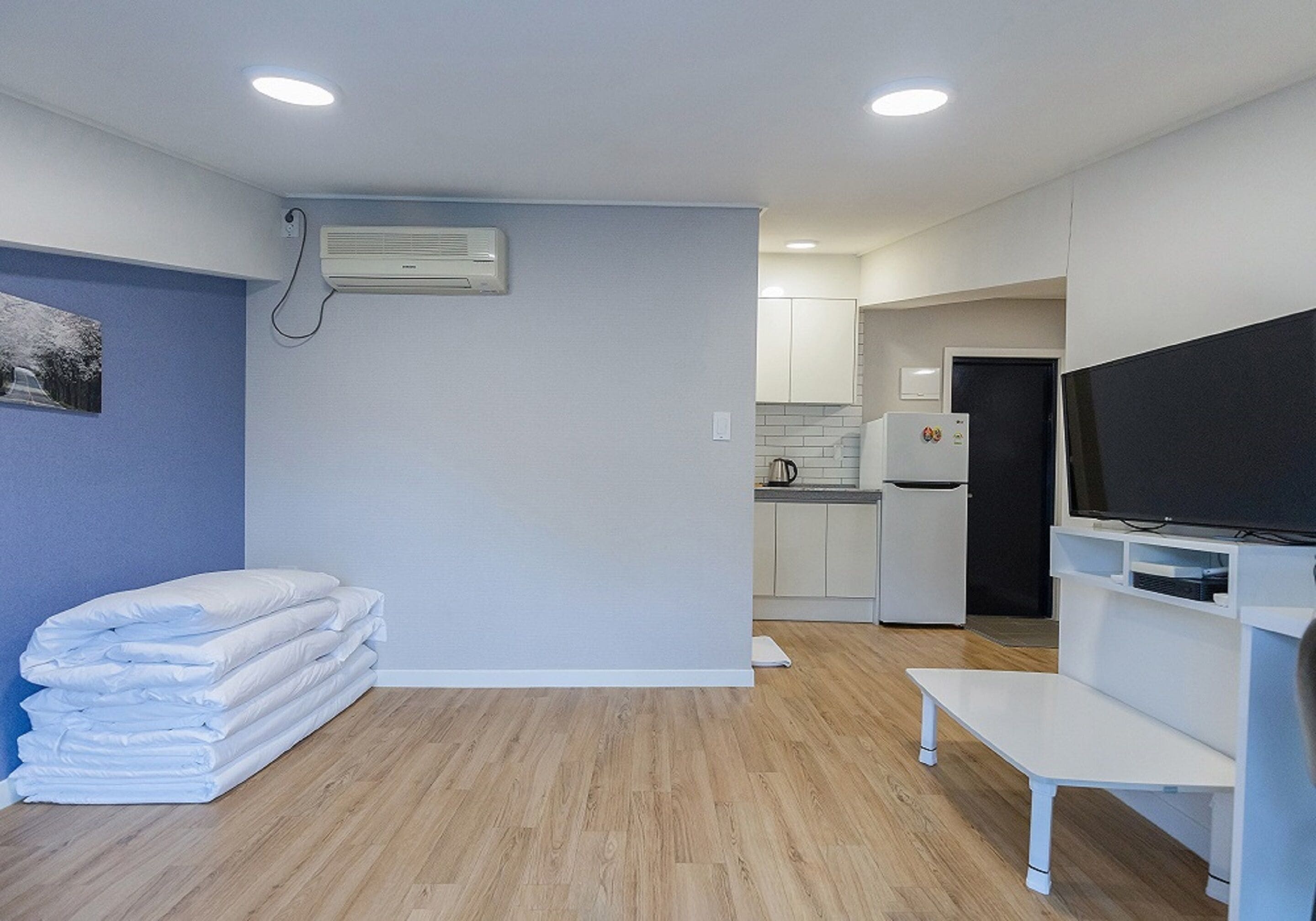 A modern, compact living space with a kitchenette, a flat-screen TV, and a stack of folded blankets.