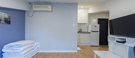 A modern, compact living space with a kitchenette, a flat-screen TV, and a stack of folded blankets.