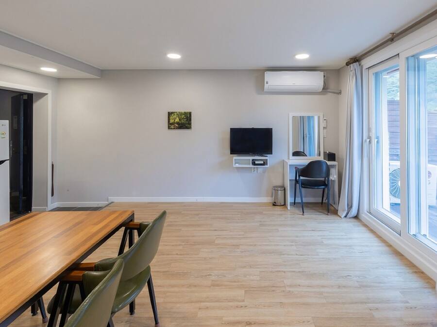 A modern kitchen with a wooden dining table and chairs, a built-in TV, and a window with curtains.
