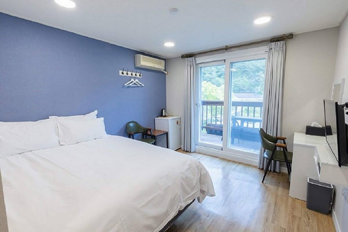 Hotelkamer met een bed, een bureau, een stoel, een tafeltje, een airconditioning en een balkon met gordijnen.