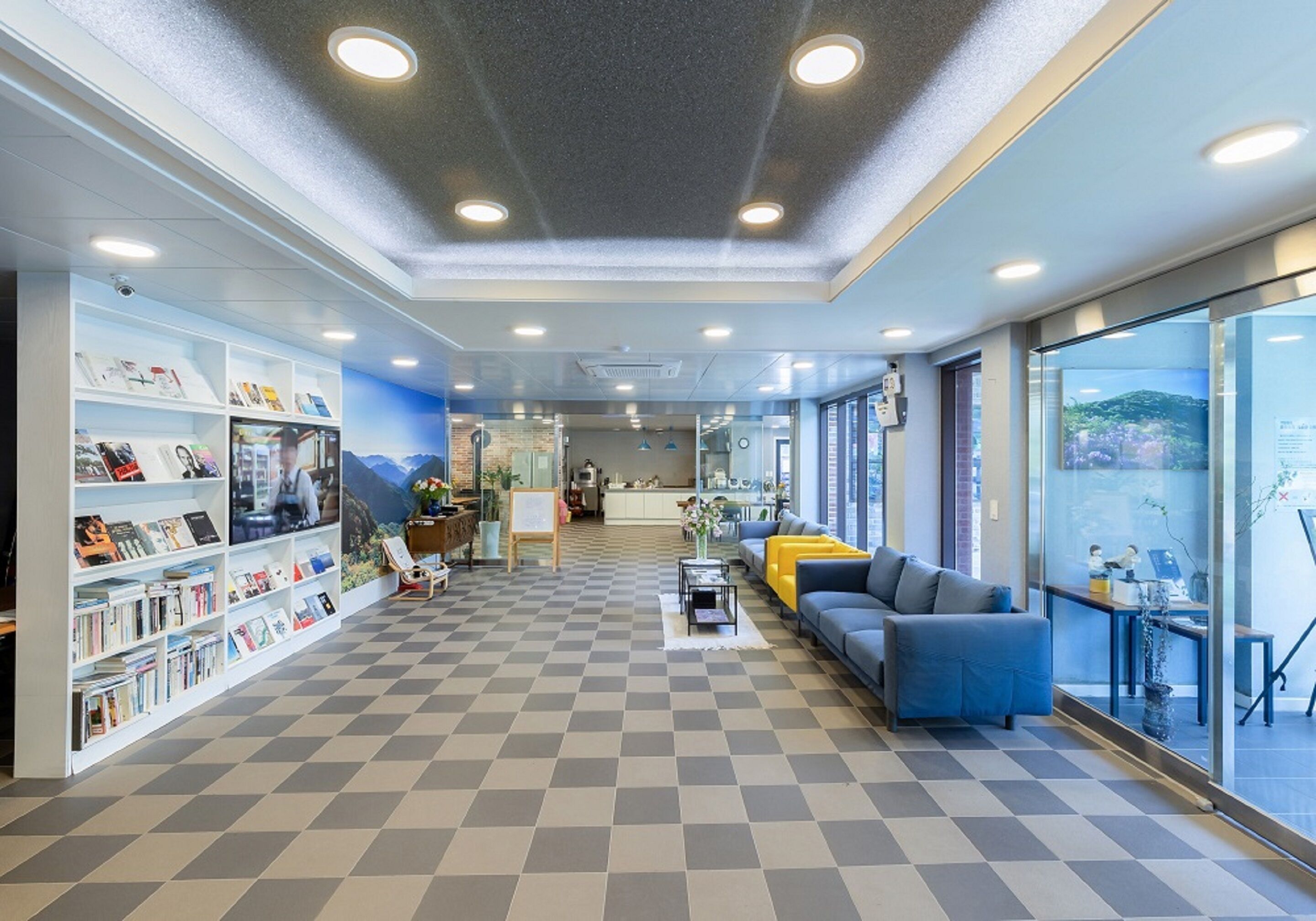 A modern interior with a checkered floor, a sofa, a bookshelf, and a view through a glass wall.