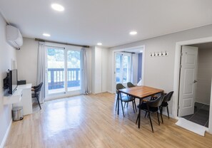 A spacious room with a wooden dining table, chairs, a TV, and a balcony with curtains. - Jirisan Parkview (Gurye)
