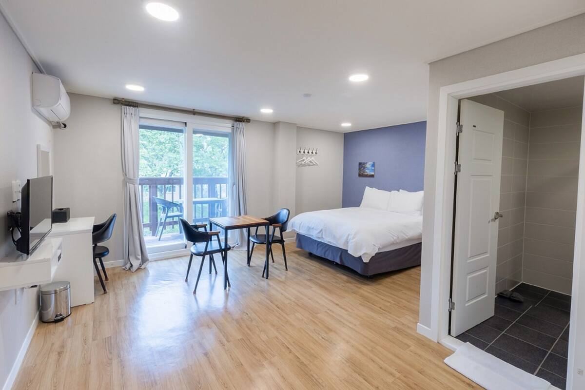 Een slaapkamer met een bed, een bureau, twee stoelen, een televisie en een raam met gordijnen.