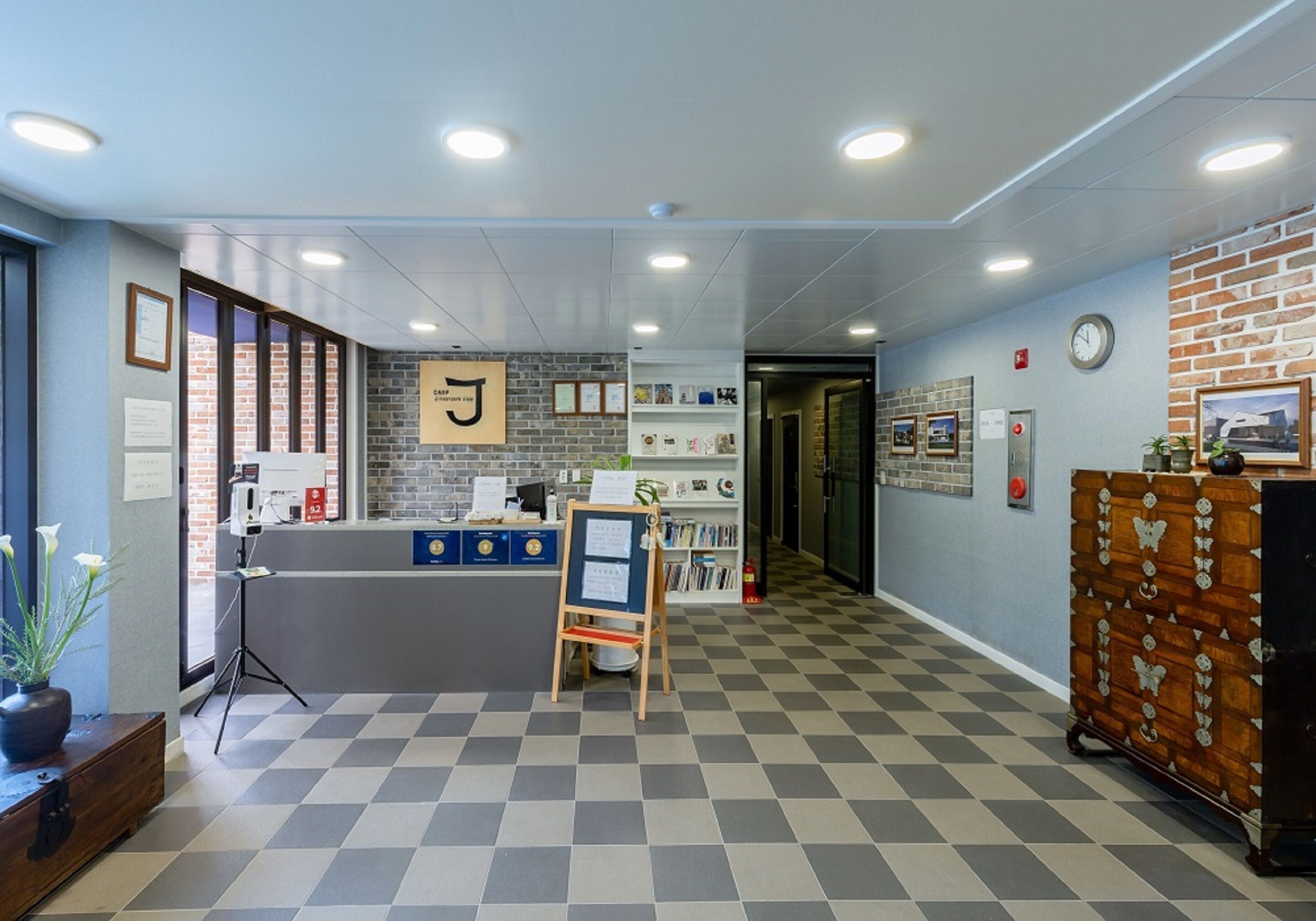 A reception area with a check-in counter, a bulletin board, a clock, and a brick wall.