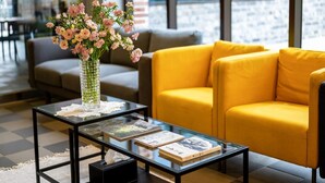 Un área de estar moderna con una mesa de centro de vidrio, un sofá amarillo y un jarrón con flores.
