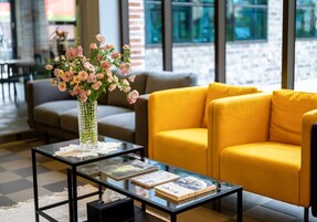 Un área de estar moderna con una mesa de centro de vidrio, un sofá amarillo y un jarrón con flores.