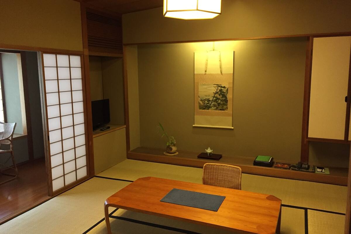 A traditional Japanese room with tatami flooring, a low wooden table, a television, and a hanging artwork.