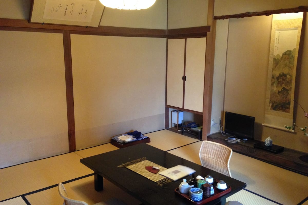 A traditional Japanese room with tatami flooring, a low table with tea sets, a chair, and a television.