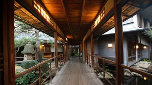 A corridor with wooden flooring and railings, leading to a traditional building with a thatched roof. - Yoyokaku (Karatsu)