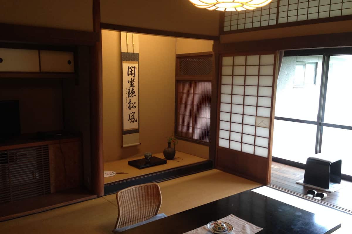 A traditional Japanese room with tatami flooring, a low table with a tea set, a shoji screen, and a hanging scroll with calligraphy.
