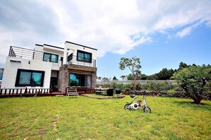 A modern two-story house with a large front yard, a patio with outdoor furniture, and a bicycle.