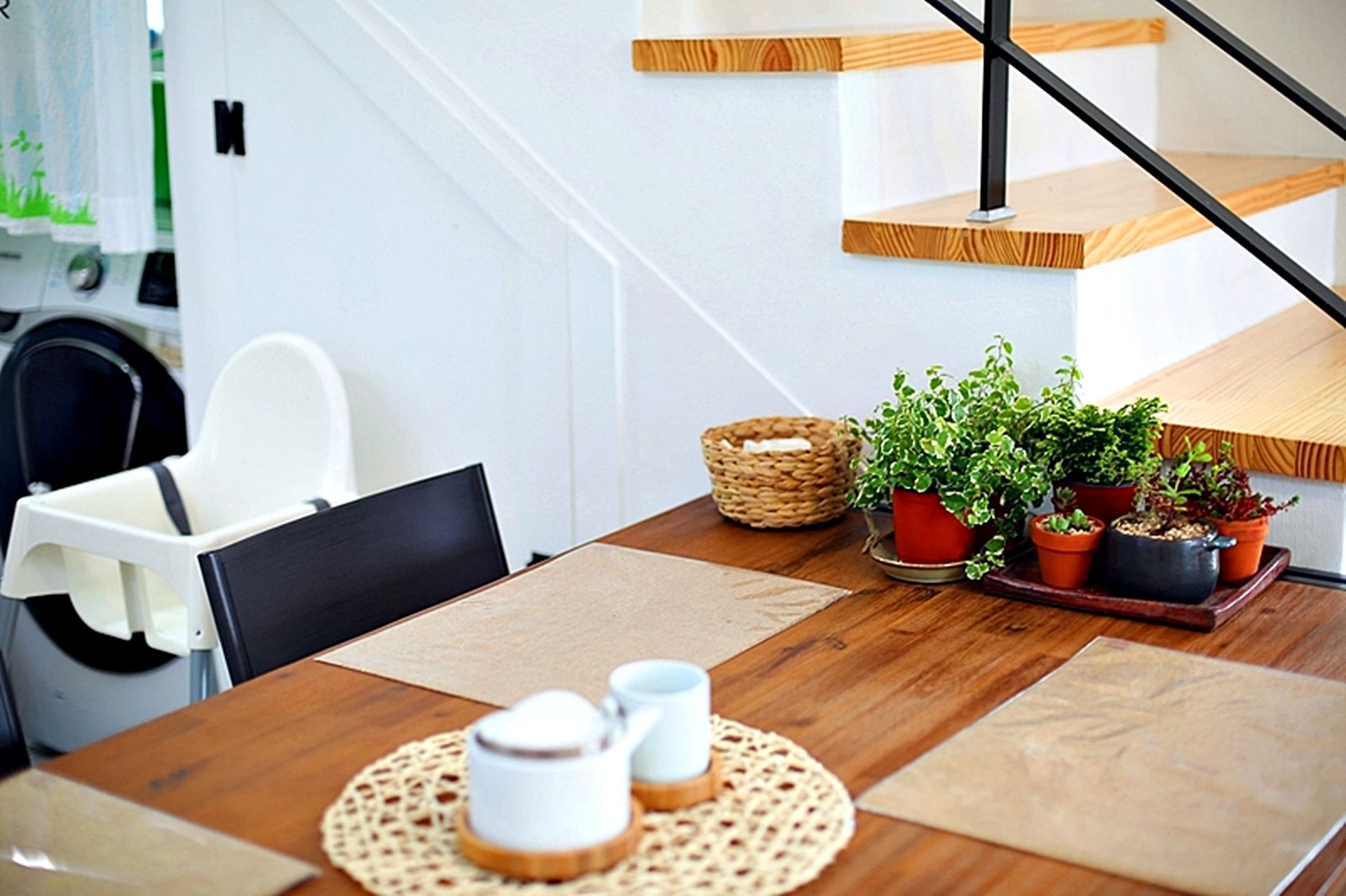 A dining area with a wooden table, chairs, a placemat, a basket, and potted plants.