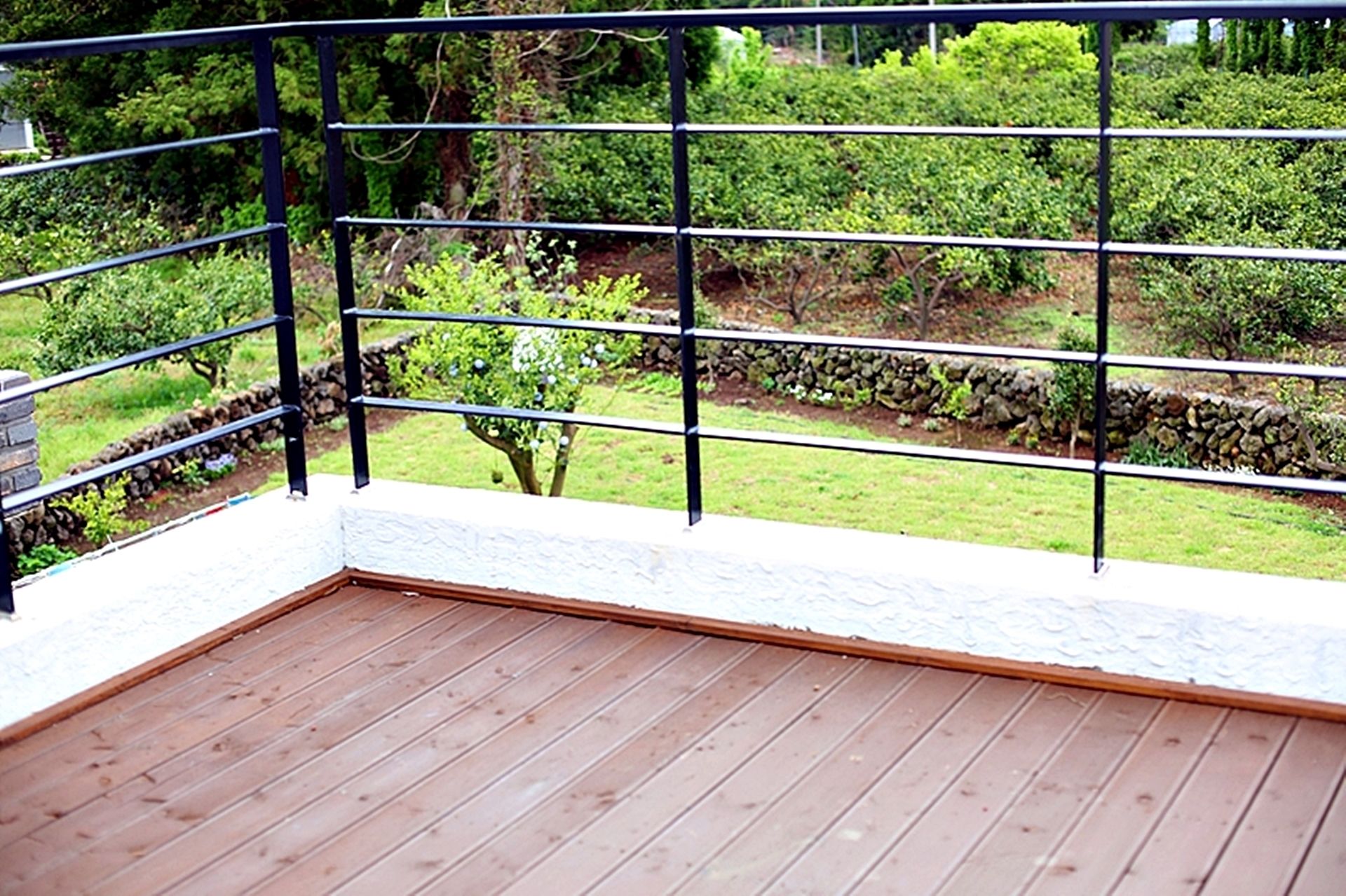 Une terrasse en bois avec une rambarde en métal donnant sur un jardin aménagé.