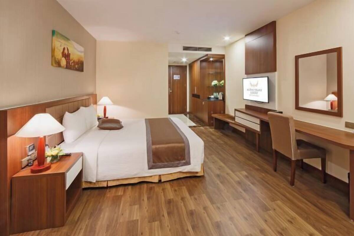 A hotel room with a bed, desk, chair, TV, and a painting on the wall.