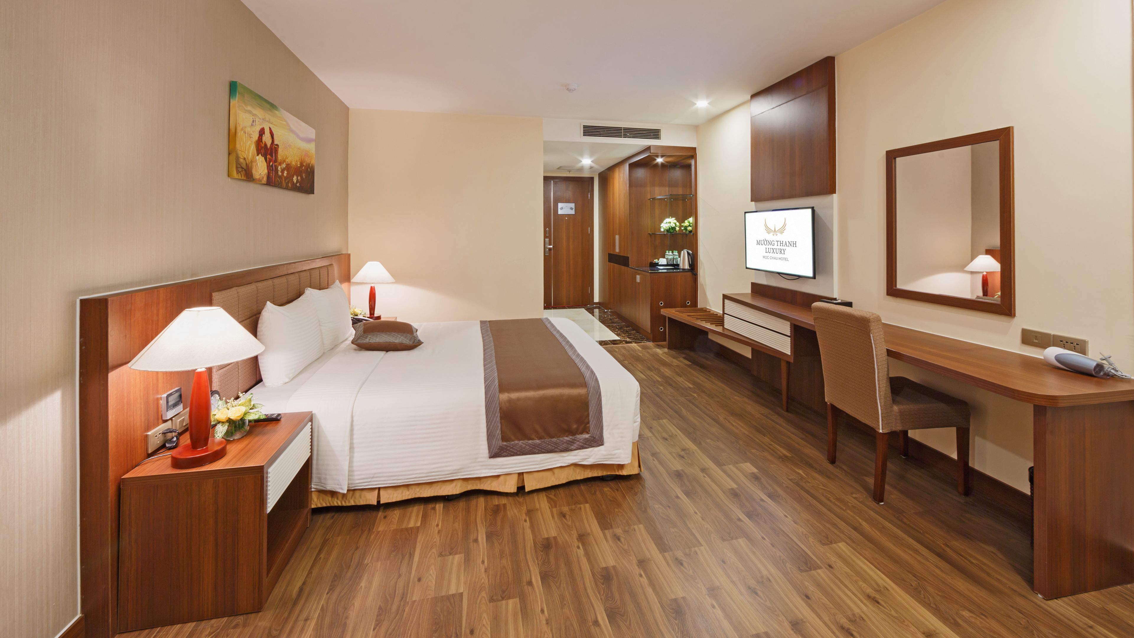 A hotel room with a bed, bedside tables, a desk, a chair, a television, and a mirror.