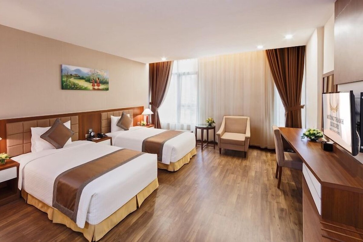 A hotel room with two beds, a desk, a chair, a TV, and a painting on the wall.