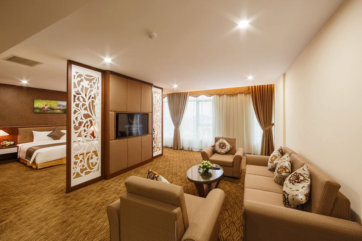 A hotel room with a bed, sofa, TV, and a decorative partition.