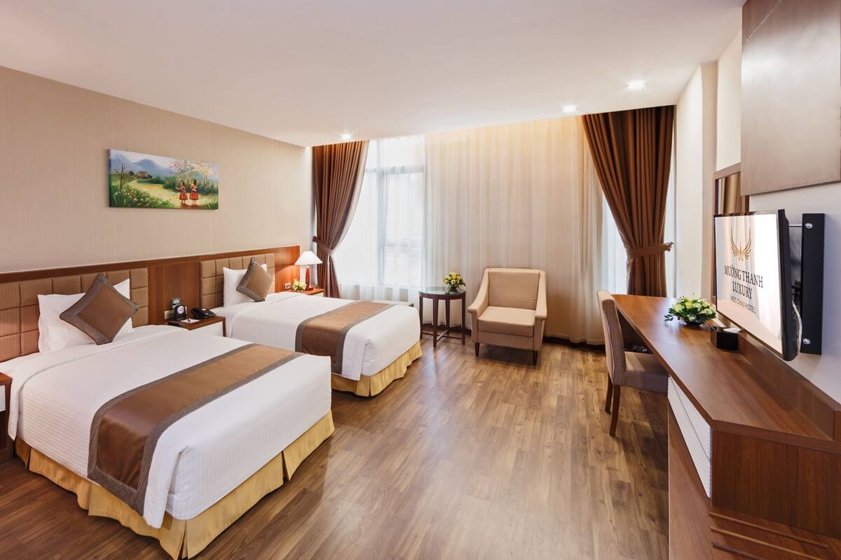A hotel room with two beds, a desk, a chair, a TV, and a painting on the wall.