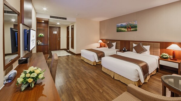 Habitación de hotel con dos camas, un escritorio de madera, una silla, un televisor y un cuadro en la pared.