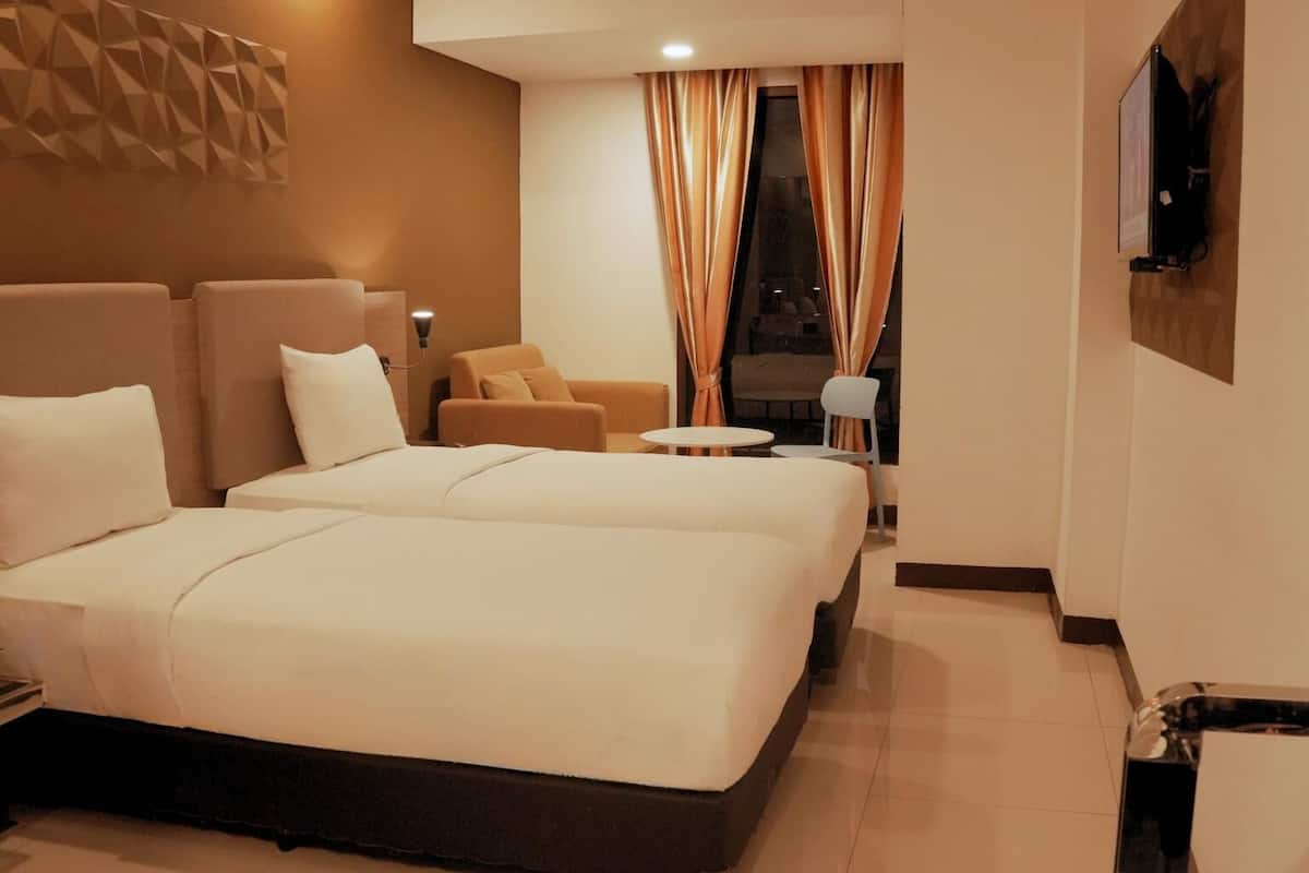 Ein Hotelzimmer mit einem Bett, zwei Sesseln, einem kleinen Tisch und einem an der Wand befestigten Fernseher.