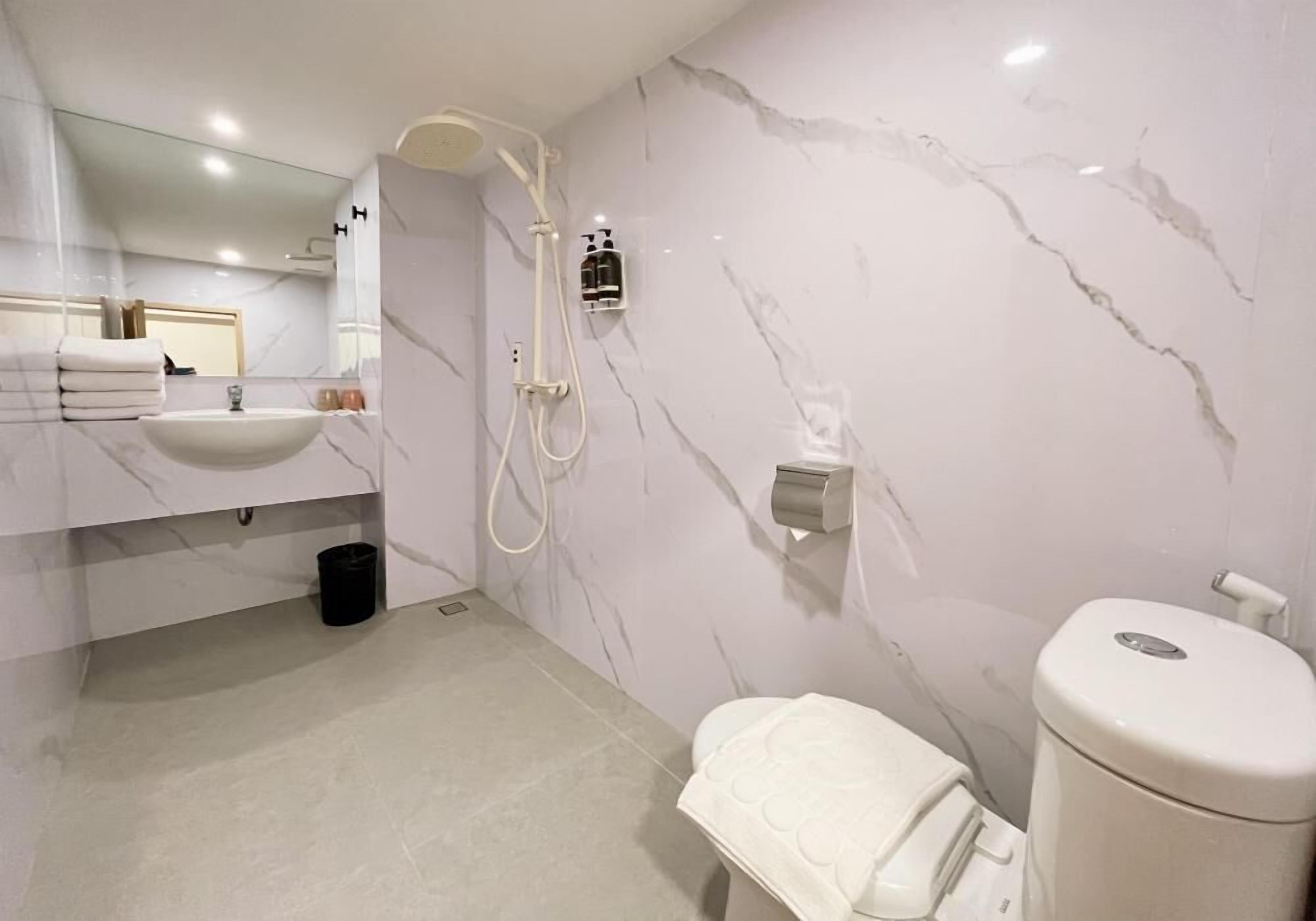 Une salle de bain moderne avec un lavabo en marbre, des toilettes, une douche et un miroir.