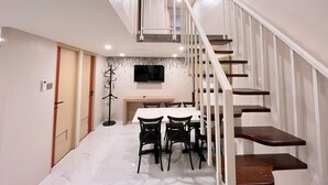 Un intérieur moderne avec un escalier, un coin repas avec des chaises, un porte-manteau et un téléviseur à écran plat fixé au mur.