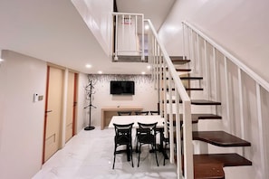 Un intérieur moderne avec un escalier, un coin repas avec des chaises, un porte-manteau et un téléviseur à écran plat fixé au mur.